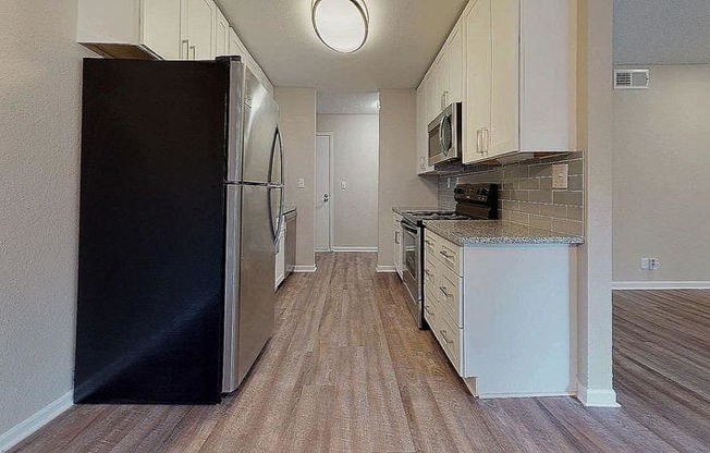 A black refrigerator is in the corner of a kitchen with wood flooring. at Spalding Vue, Peachtree Corners, 30092