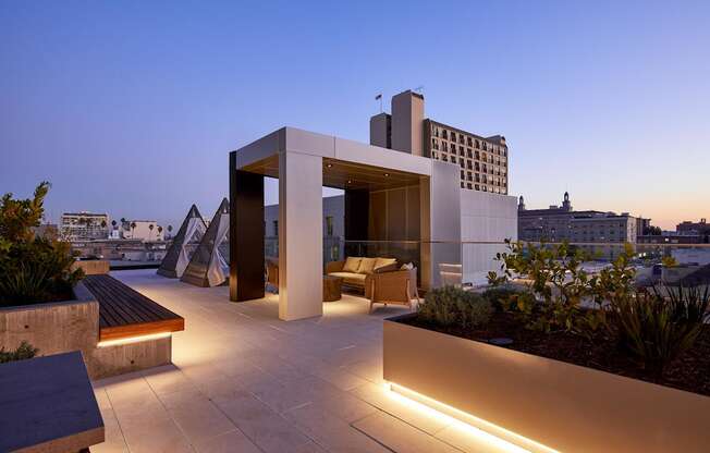 A modern building with a unique design is illuminated by lights at dusk.