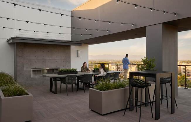 A rooftop patio with people sitting at tables and a view of the city.