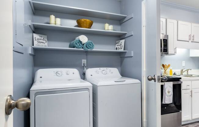 a white washer and dryer in a small laundry room with shelves