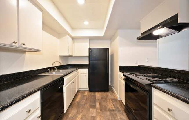 a kitchen with black counters and white cabinets and a black refrigerator