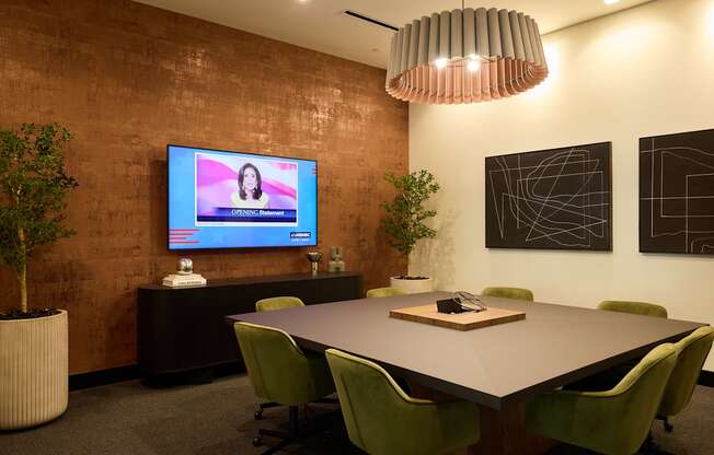A conference room with a large table, chairs, and a television screen displaying a woman's face.
