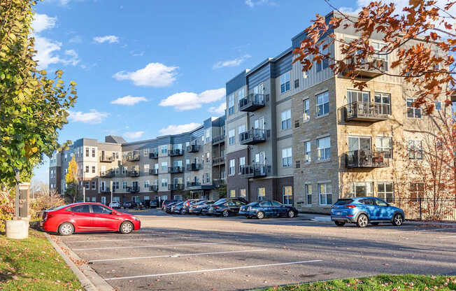A red car is parked in a parking lot in front of apartment buildings.