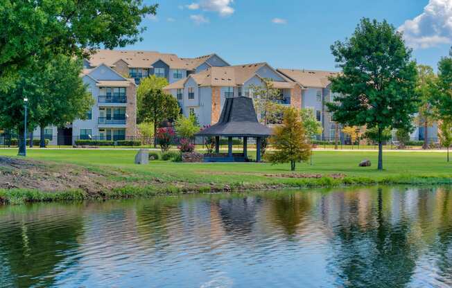 a gazebo sits on the edge of a lake in front of an apartment complex