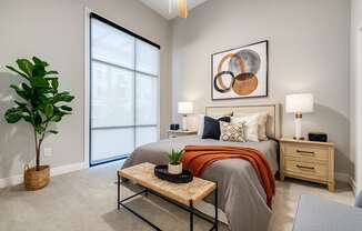 A bedroom with a bed, nightstand, and a plant.