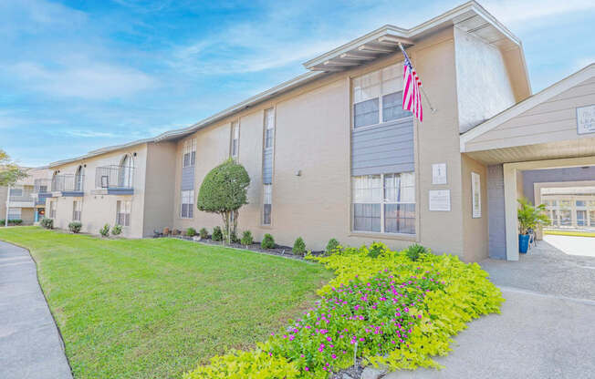 An apartment building with an American flag and a path leading to the leasing office at The Creole Apartments in Shreveport, LA