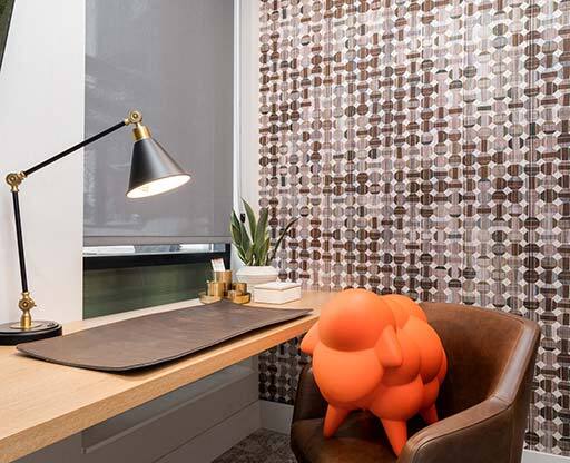 A chair with an orange design on it sits in front of a desk with a lamp on it.