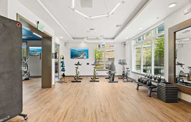 A gym with a variety of exercise equipment and a view of the outdoors through the windows.