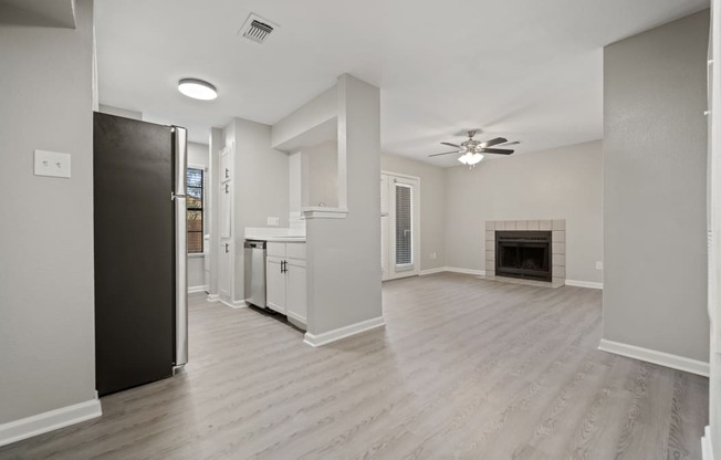 an empty living room with a kitchen and a fireplace