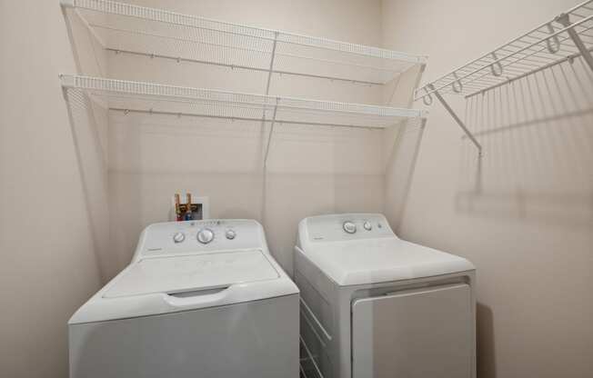 two washers and dryers in a laundry room with a shelf above them