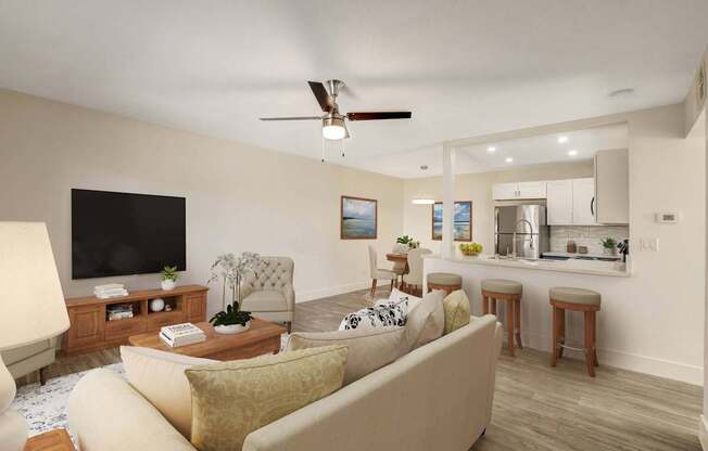 A living room with a beige couch, a wooden coffee table, a flat screen TV, and a kitchen area in the background.