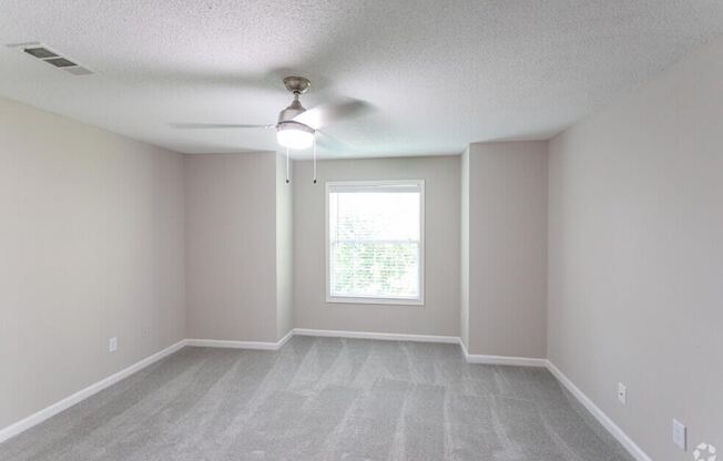 an empty living room with a ceiling fan and a window