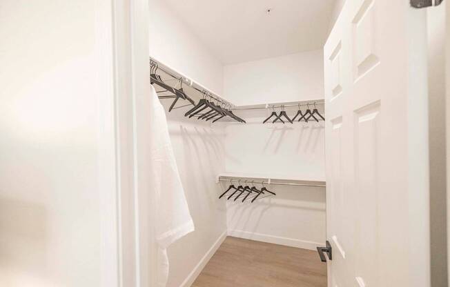 A white closet with clothes hanging on hangers.