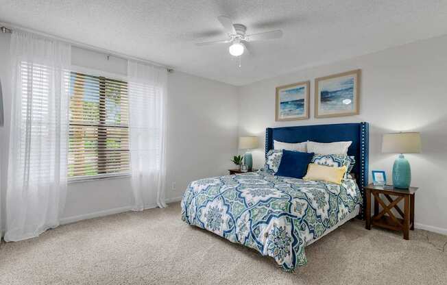 A bedroom with a bed, a ceiling fan, and a window with blinds.