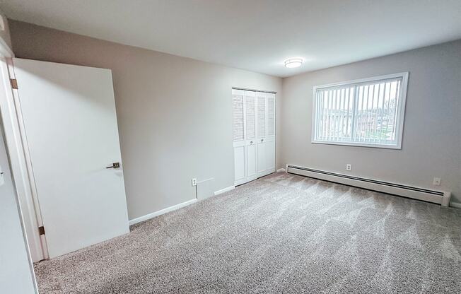 A room with a carpeted floor and a window with blinds.