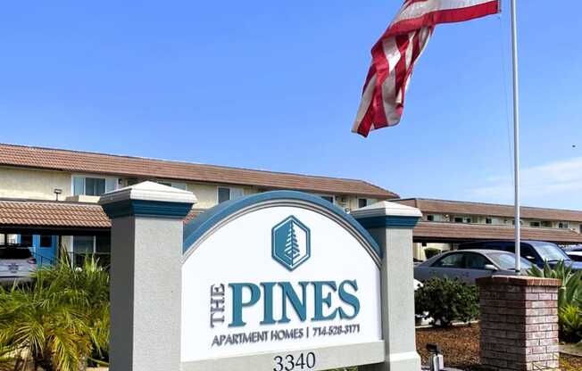 an flag flies above the pines apartments sign in front of a building