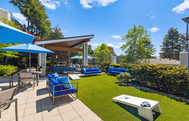 a patio with blue chairs and umbrellas and a lawn