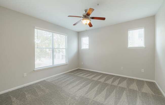 an empty living room with a ceiling fan and two windows