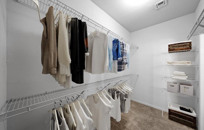 A white walk in closet with clothes hanging on racks.