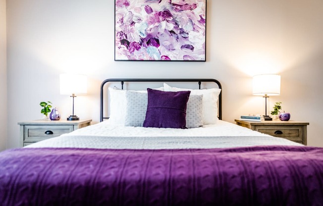 a bedroom with a bed with a purple blanket and white bedding
