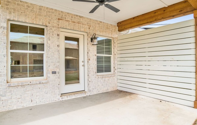 an empty porch of a brick house with a white door and a ceiling fan