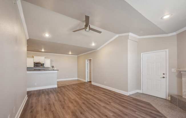 an empty living room with a ceiling fan and a kitchen