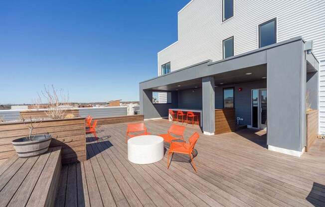 A modern deck with orange chairs and a white table.