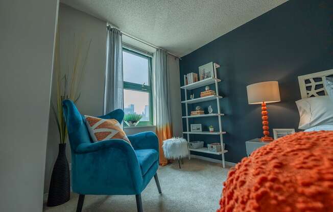 a bedroom with a blue chair and orange bedspread