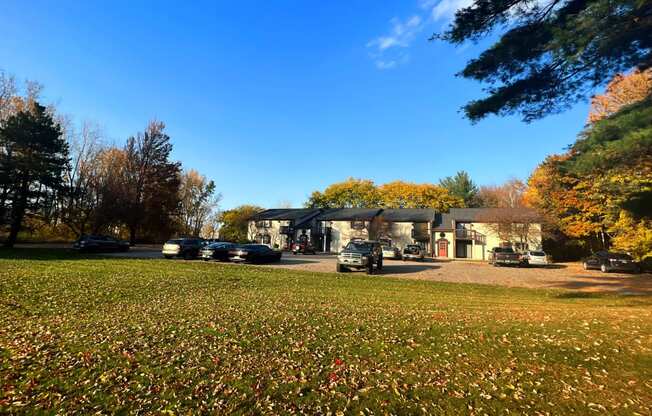 a house in the middle of a grassy field with cars parked in front of it