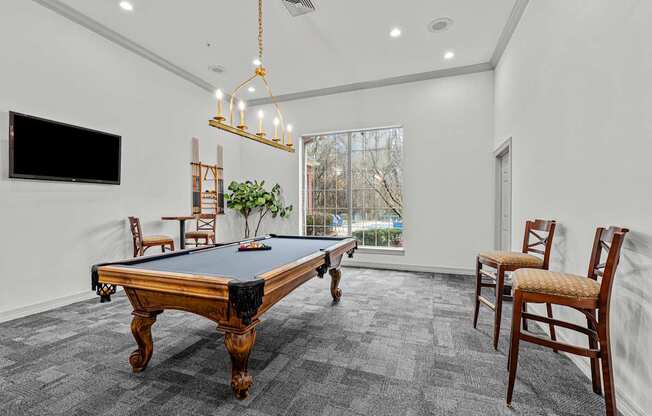 A pool table is in the middle of a room with chairs and a television.