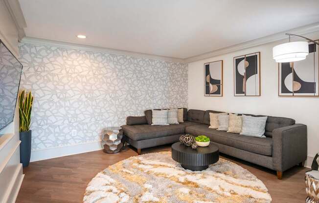 A living room with a grey couch, a coffee table, and a patterned wallpaper.