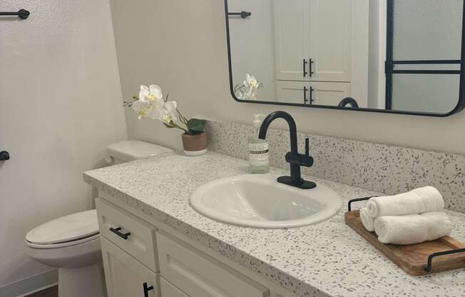 A bathroom with a white toilet and a sink with a black faucet. at Camino de Oro Apartments, Torrance, CA, 90505