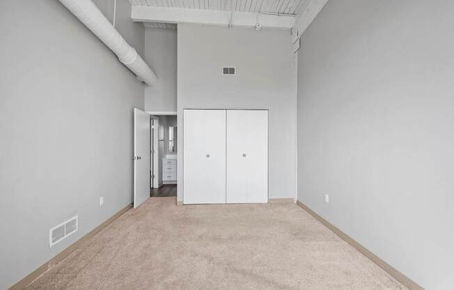 A room with white walls and carpeted floor with a white door in the middle.