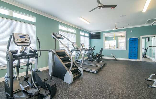 two treadmills and other exercise equipment in a gym with windows