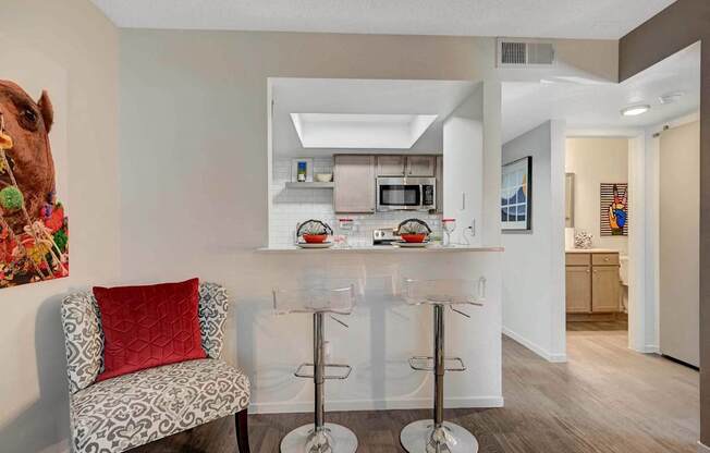 A kitchen with a bar stool and a chair with a red pillow.