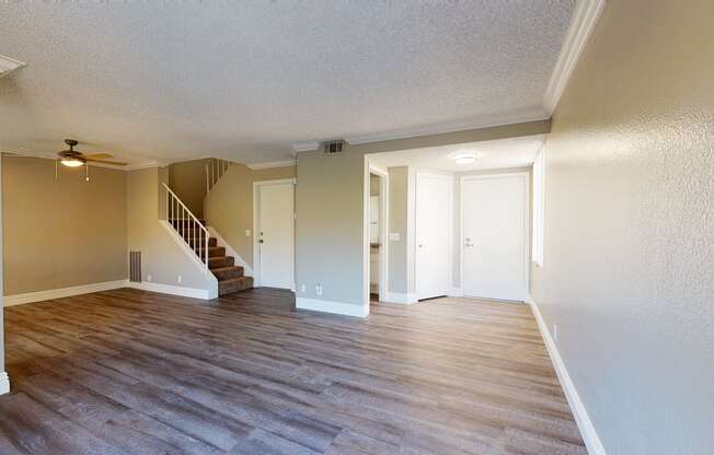Apartments in Ontario CA - Rancho Vista - Unfurnished Living Room With Wood Styled Flooring, a View of the Dining Room, and Adjacent Entryway and Guest Bathroom