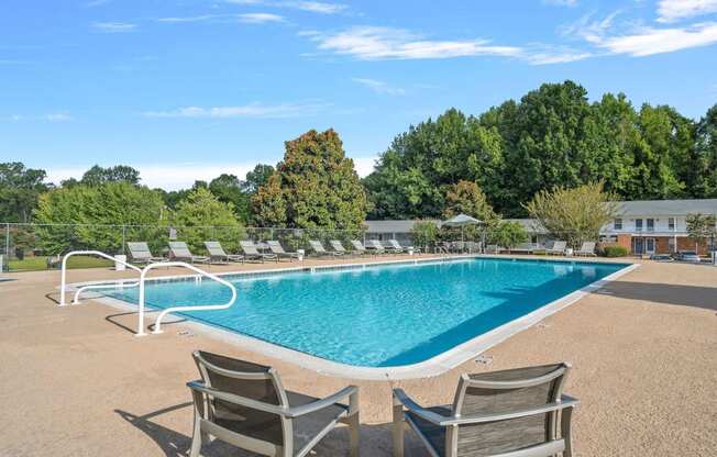 a swimming pool with chairs around it and trees in the background