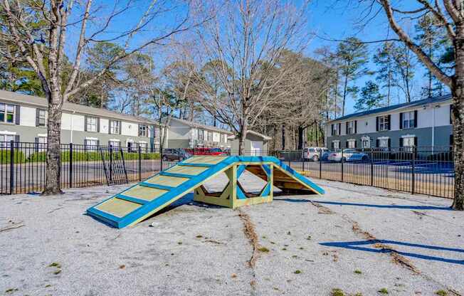 A playground with a blue and yellow slide in the foreground and apartment buildings in the background.
