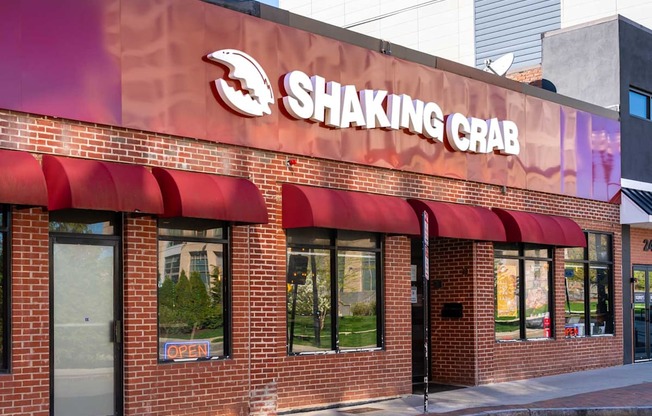 The exterior of a Shaking Crab restaurant with a red awning and a blue sign on the window.