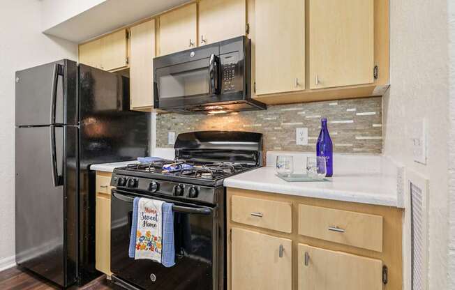A kitchen with a black refrigerator and stove top oven.