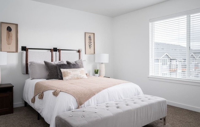 a bedroom with a bed and an ottoman in front of a window