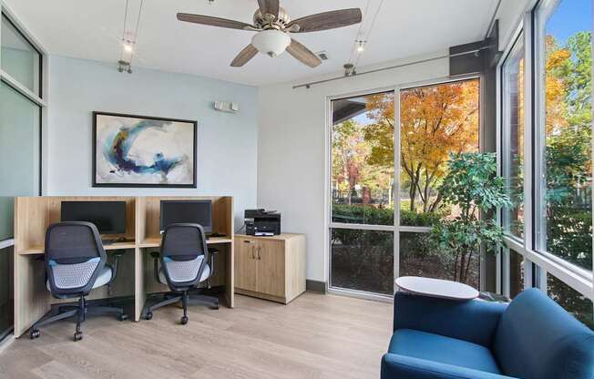 A room with a ceiling fan, two chairs, a desk, and a painting.