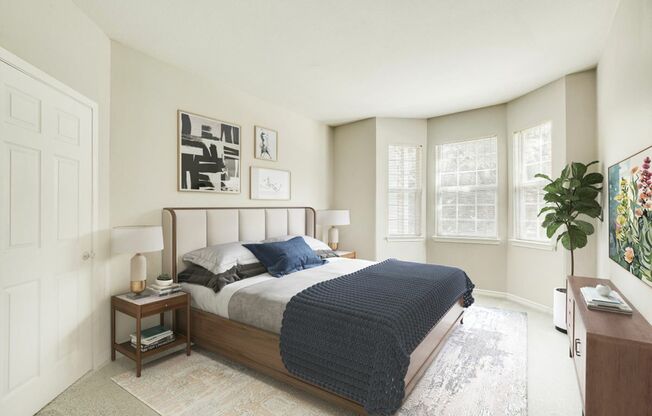 View of Cottonwood Ridgeview Bedroom Model showing King-Sized Bed, Large Bay Windows, Two Night Stands With Lamps, and a Large Flat Screen TV and Console