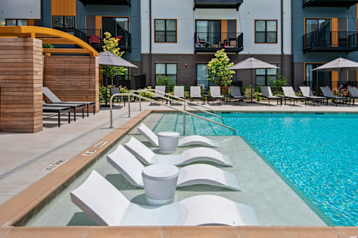 a swimming pool with lounge chairs and umbrellas in front of a building