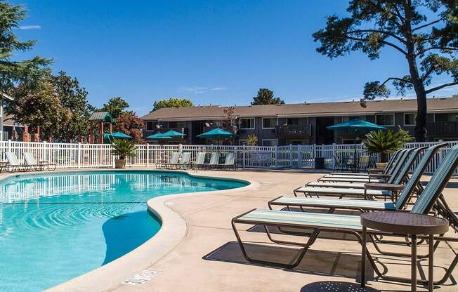 A pool area with sun loungers and a building in the background.