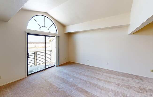 A living room with a cathedral ceiling and large window and sliding glass doors to a balcony at South Bridge Apartments in Fort Wayne, Indiana