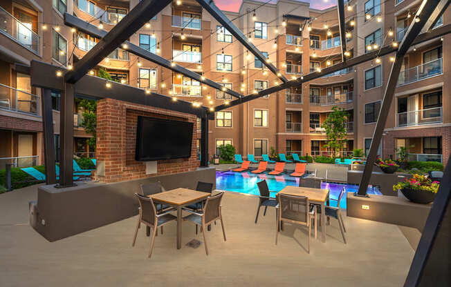 A modern outdoor patio area with a television, seating, and a pool.