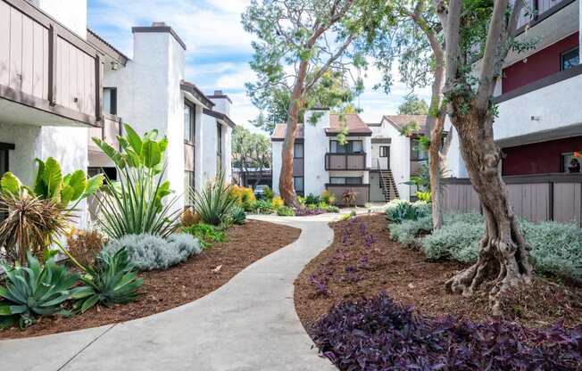 Fusion Warner Center apartments in Woodland Hills pathway between two-story buildings with lush green landscaping and brown bark mulch.