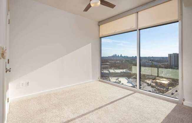 an empty living room with a large window and a ceiling fan