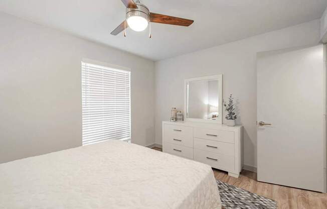 A white bedroom with a bed, dresser, mirror, and a ceiling fan.